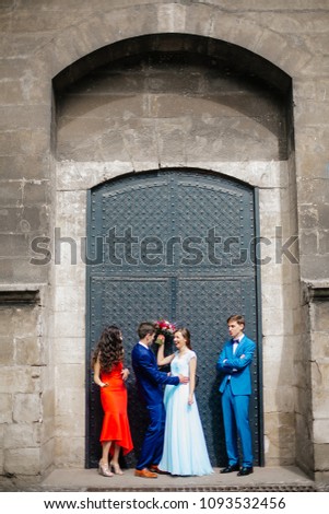 Full length portrait of newlywed couple dancing and having fun with bridesmaids and groomsmen in the old city center. Bride and groom with friends posing near old door and wall. Funny Wedding moments.