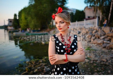 A beautiful young woman dressed standing by the lake.