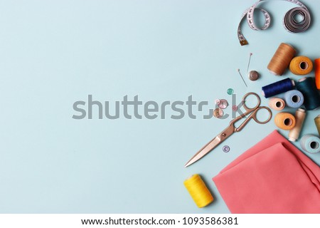 Sewing accessories and fabric on a blue background. Sewing threads, needles, pins, fabric, buttons and sewing centimeter.
 top view, flatlay Royalty-Free Stock Photo #1093586381
