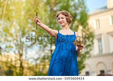 Beautiful girl-artist on the street in a blue dress, smiling, with tassels and palette in her hands for any purpose