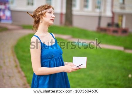 Beautiful girl-artist on the street in a blue dress writing something in a notebookl for any purpose