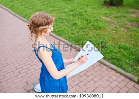 Beautiful girl-artist on the street in a blue dress draws a sketch of the picture 