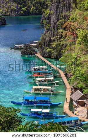 The view of wooden pier with anchored boats on azure clear sea near Kayangan lake, Coron Island