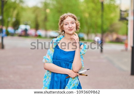 Beautiful girl-artist on the street in a blue dress, smiling, with tassels in her hands