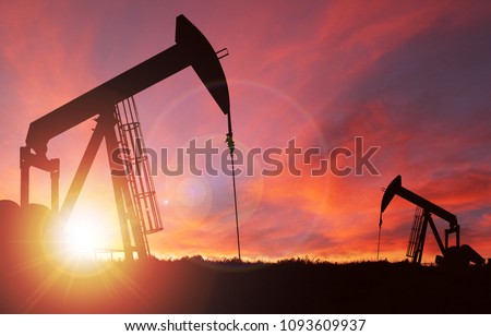 Pump jack silhouette against a sunset sky with deliberate lens flare and copy space. These jacks can extract between 5 to 40 litres of crude oil and water emulsion at each stroke.