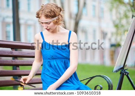 Beautiful girl-artist on the street in a blue dress, draws on the easel