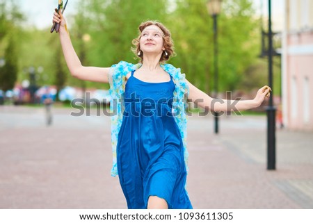 Beautiful girl-artist on the street in a blue dress, smiling, with tassels in her hands 