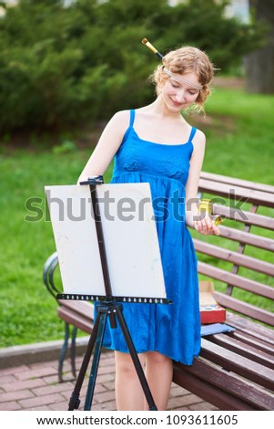 Beautiful girl-artist on the street in a blue dress, draws on the easel 