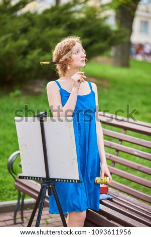 Beautiful girl-artist on the street in a blue dress, draws on the easel