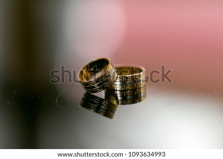 A closeup image with two beautiful golden wedding rings reflecting into a mirror table in a beautigul sunlight with different shadows and shades of white,black and red on the table