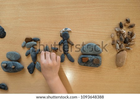 The child is playing with stones from children’s activities.kid draws a people,home and tree for her handcraft 
picture.