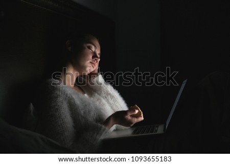young girl sitting in bed late at night and watching a boring movie on her laptop, falling asleep