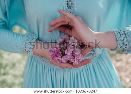 pink flowers in the hands of a girl who is dressed in a blue dress