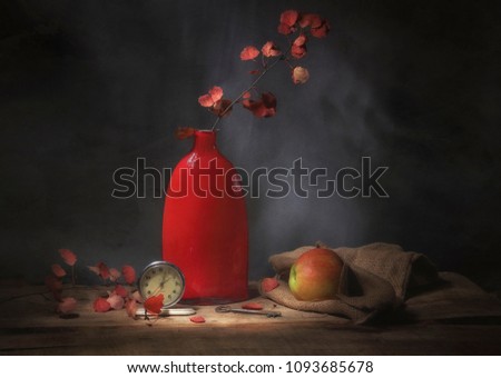 
Classic still-life with a red vase, an apple, autumn leaves and  an alarm clock. Art photography.