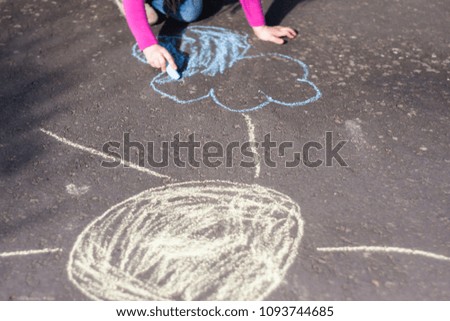 Little child is drawing a landscape onto the sidewalk