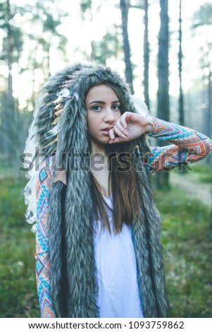 Portrait of young dramatic girl with Indian feather hat roach in forest