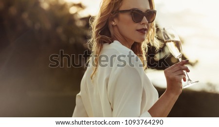 Attractive woman in sunglasses drinking wine outdoors. Beautiful female having a glass of wine looking backwards. Royalty-Free Stock Photo #1093764290