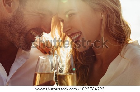 Close up of a romantic couple with their heads together holding a glass of wine. Couple with wine smiling outdoors. Royalty-Free Stock Photo #1093764293