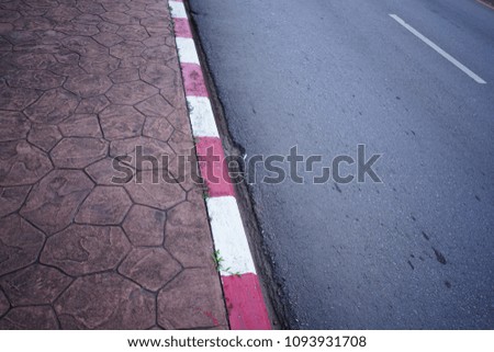 The brown sidewalk with red and white lines . Meaning that they can not stop or parking the car beside of the concrete road.