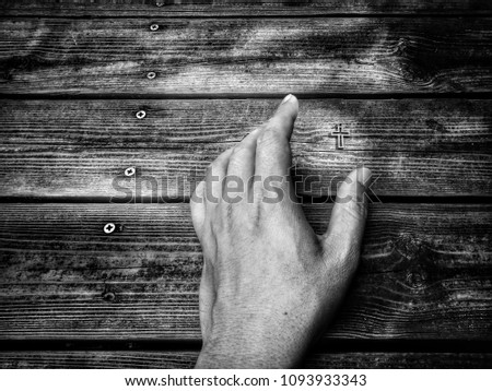 Hand with christian cross on vintage wooden background, image with selective focus and monochrome process