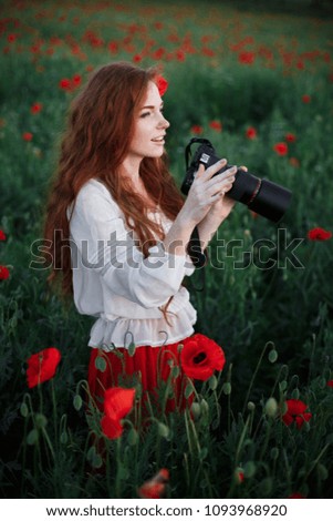 Girl taking picture on a professional camera in a poppy field