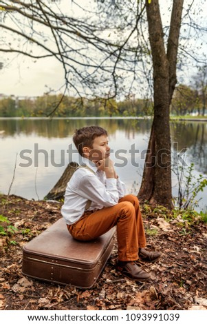 a brooding rustic simpleton fellow sitting on a retro old-fashioned suitcase on the bank of a river lake Royalty-Free Stock Photo #1093991039