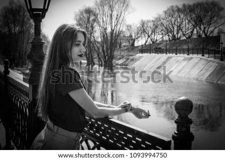 Fashionable beautiful woman in a black jacket on a summer day against the background of the city river Royalty-Free Stock Photo #1093994750