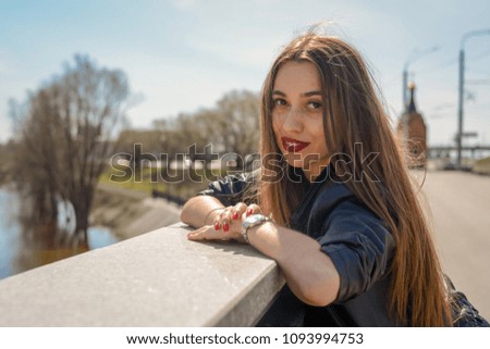 Fashionable beautiful woman in a black jacket on a summer day against the background of the city river Royalty-Free Stock Photo #1093994753