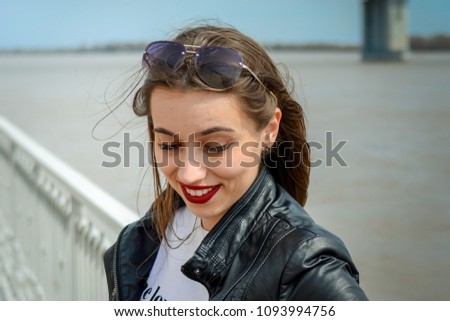 Fashionable beautiful woman in a black jacket on a summer day against the background of the city river Royalty-Free Stock Photo #1093994756