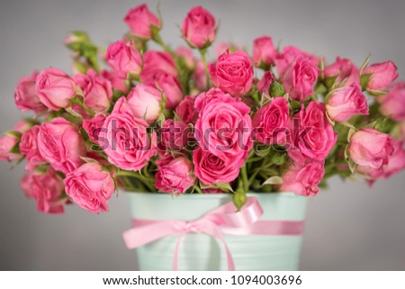 small Bush pink roses in a mint-colored pot on a gray background