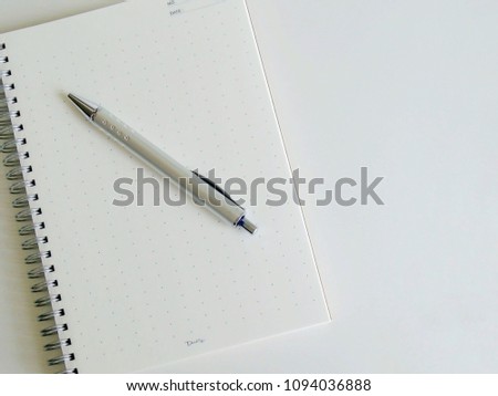 Blank notebook paper with a silver pen on white background.Top view.