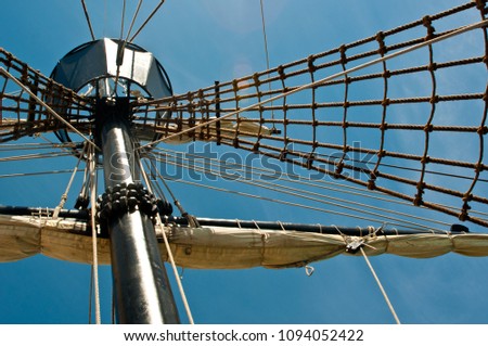 Antique sailing ship mast crows nest with rigging against blue sky Royalty-Free Stock Photo #1094052422