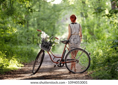 a girl in a white dress is standing and looking next to a red bicycle with a basket and flowers
