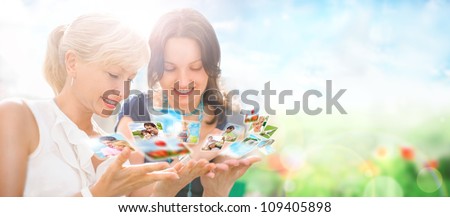 Portrait of two happy women mother and daughter looking their photo and video files in social media resources using virtual interface of future. Outdoors at beautiful idyllic place.