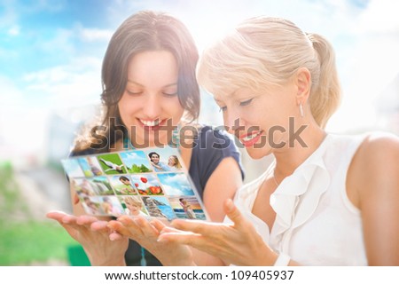 Portrait of two happy women mother and daughter looking their photo and video files in social media resources using virtual interface of future. Outdoors at beautiful idyllic place.