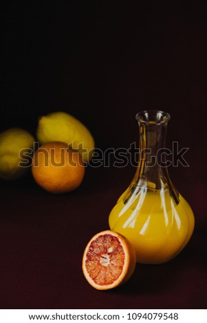 Fresh orange juice in a glass bottle on burgundy fabric on a black background with lemons, dark food photo