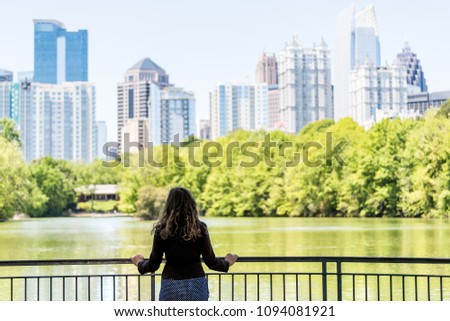 Young woman standing in Piedmont Park in Atlanta, Georgia looking at scenic water, and cityscape skyline of urban city skyscrapers downtown, Lake Clara Meer