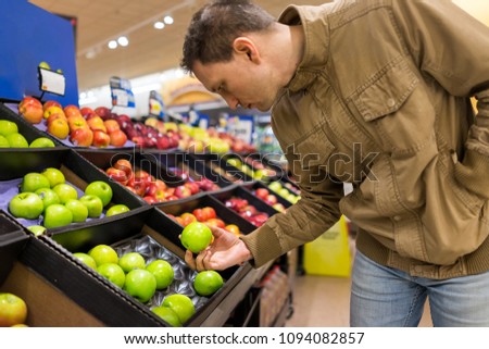 Many varieties assorted apples on display shelf in grocery store boxes in aisle, supermarket inside, man person customer holding choosing granny smith green fruit