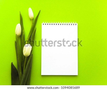 Bouquet of tulips and notebook on green background. Flat lay. Top view.