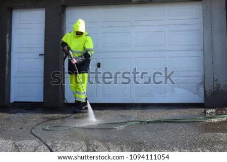 A man washes the asphalt with water. The jet of water is supplied under pressure. Flying splashes, dust and small rubbish.