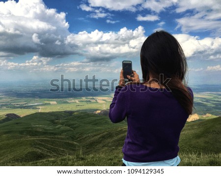 Beautiful young woman taking a shot of valley with smartphone