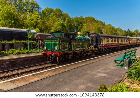 A train passing through a station on a railway line in the UK on a sunny summer day