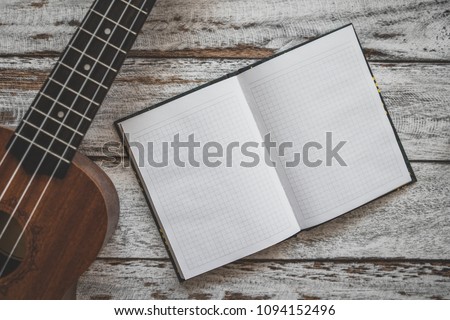 Ukulele guitar and notebook on wooden desk