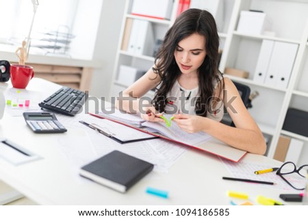 Beautiful young girl sitting at an office desk holding a pen in her hand and tearing off a bright sticker.