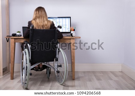 Rear View Of A Disabled Businesswoman Sitting On Wheelchair Working On Computer