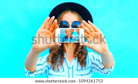 Cool girl is taking photo self portrait on a smartphone in the city closeup screen over colorful blue background