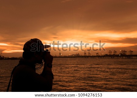 Silhouettes of man taking a photo construction site next to the sea in the sunset.