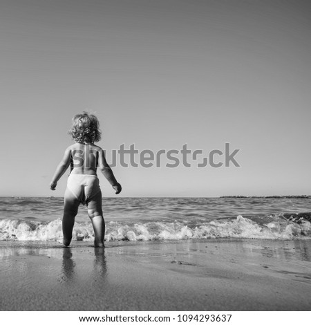 Happy kid having fun. Childhood. Baby boy one cute fair-haired blond kid tiny little child back view walking on sea water waves wet sand sunbathing on warm sunny summer day bright blue sky on seascape