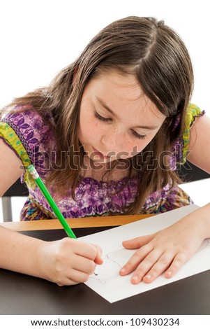 Cute 10 year old girl student drawing a picture at a desk isolated on white