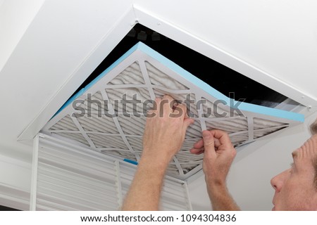 Person removing an old dirty air filter from a ceiling intake vent of a home HVAC system. Unclean gray square furnace air filter being taken out of a ceiling air vent. Royalty-Free Stock Photo #1094304836